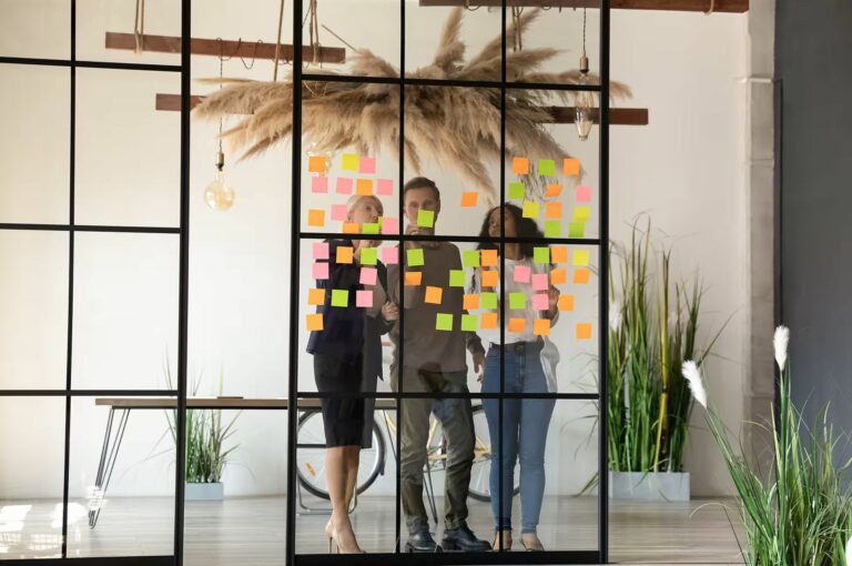 Une équipe organise son travail sur une paroi vitrée couverte de notes